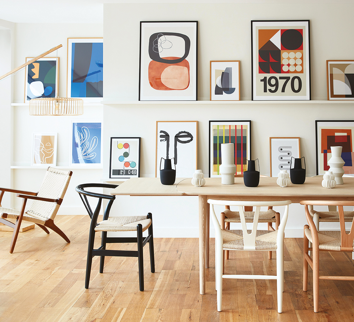 Image of a leaning gallery of art behind wishbone-style wooden dining chairs, Cultfurniture.com